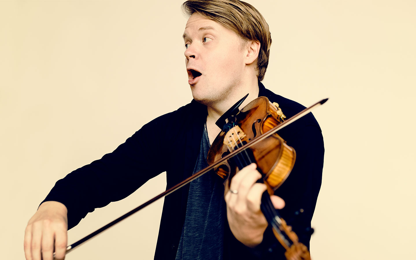 Pekka Kuusisto playing violin in front of a light yellow background