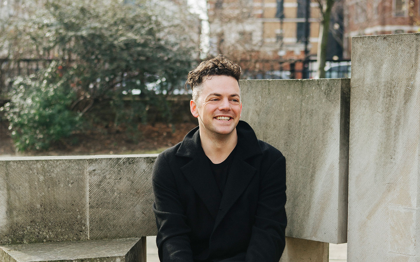 A portrait of Nico Muhly sitting on a wall