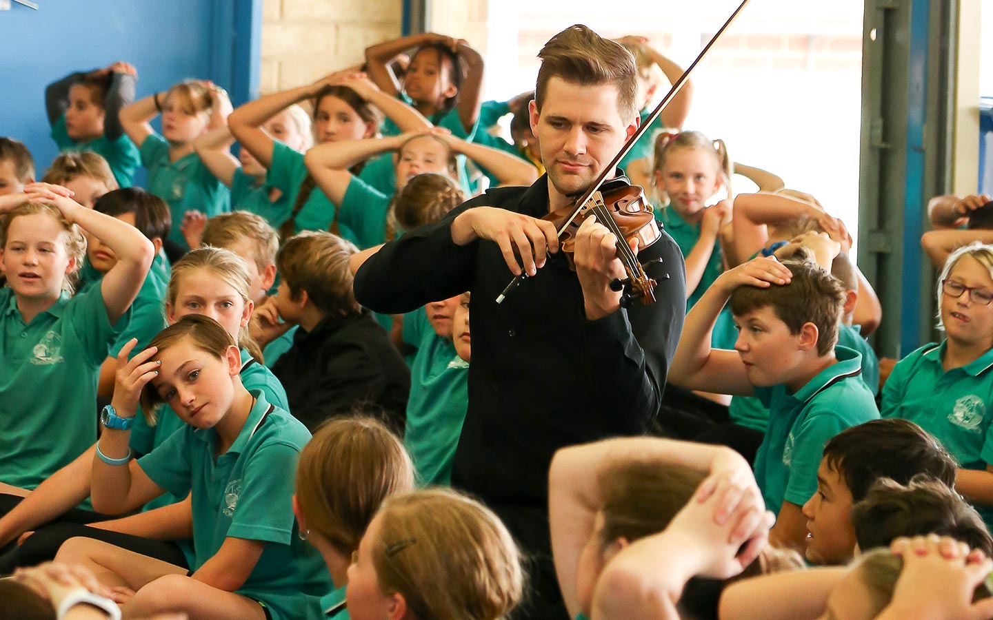 A violinist performing among a large group of primary school students