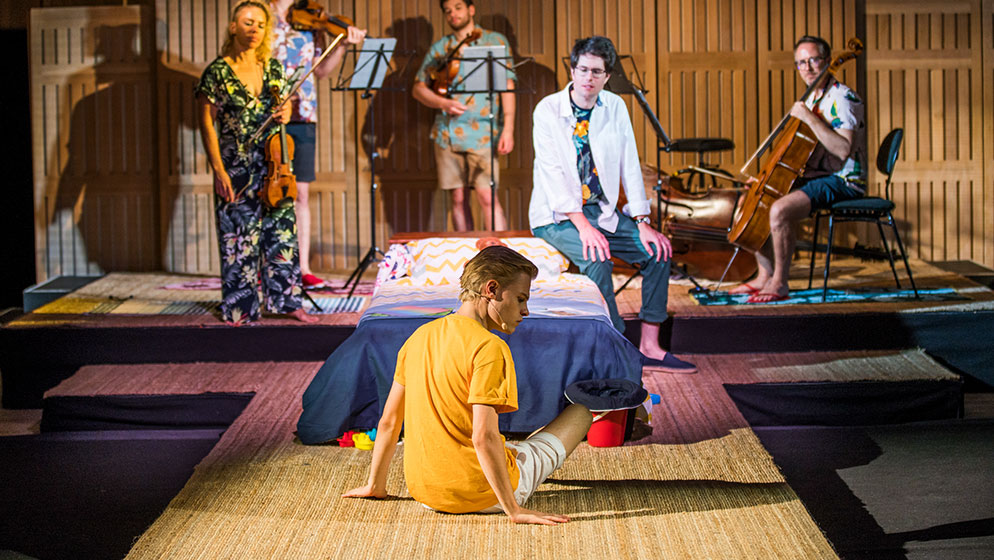 An actor sitting in front of a bed while rehearsing 'There's a Sea in my Bedroom'