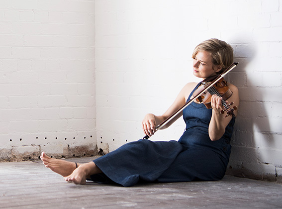 Satu Vänskä sitting on the ground playing a Stradivarius violin
