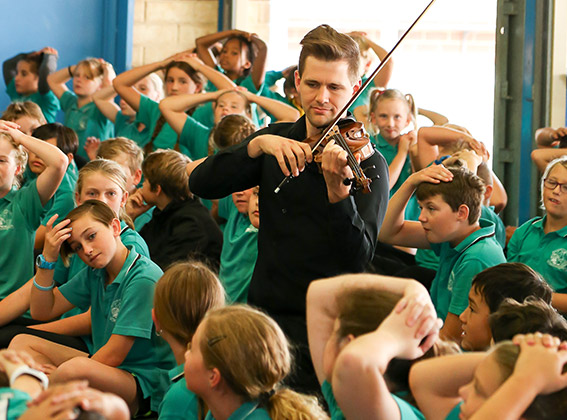 A violinist performing among a large group of primary school students